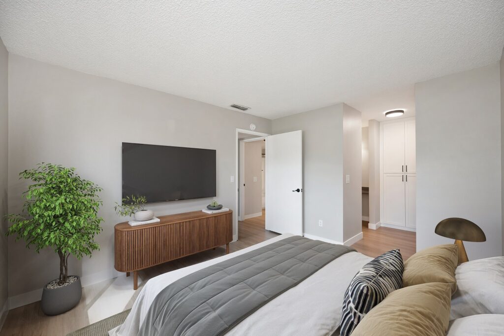 Renovated apartment bedroom with bed, television above dresser, and open linen closet.