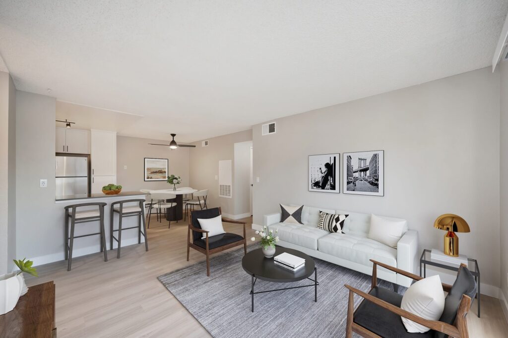 Living room with couch, two arm chairs, black and white photographs behind the couch, and view of the kitchen and dining area in renovated apartment.